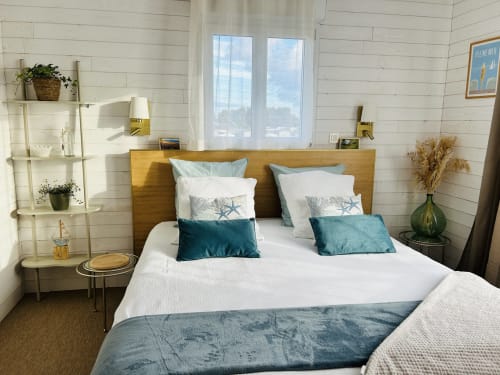 Chambre bord de mer à La Villa Plein Vent avec tête de lit en bois, oreillers bleu océan, murs en lambris blanc et vue sur le jardin