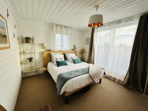 Chambre lumineuse à La Villa Plein Vent avec murs en lambris blanc, lit en bois, fenêtres sur jardin et éclairage suspendu