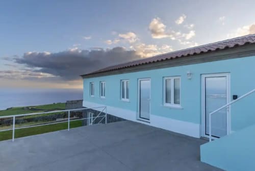Hotel Ti Chôa em Serreta: edifício moderno azul claro com vistas do oceano sob céu nublado dramático