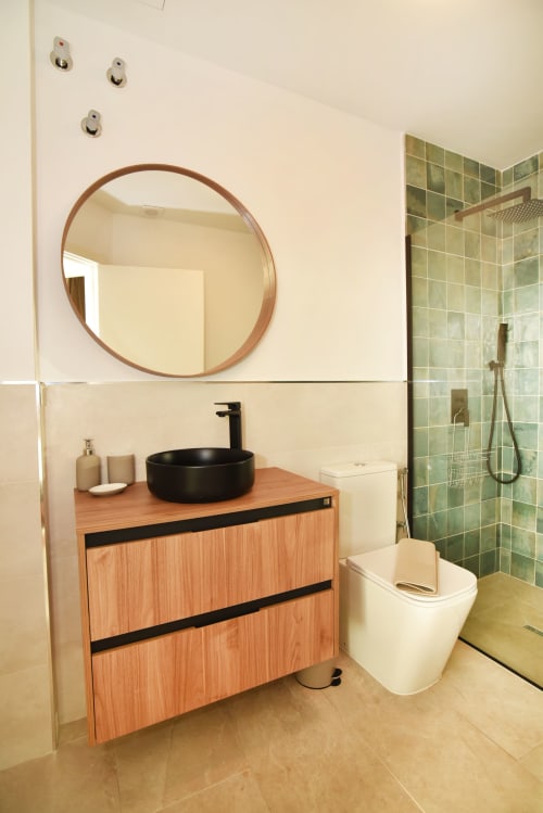 Baño moderno en Sunset House, El Cotillo con vanidad de madera, lavabo negro de cerámica, espejo redondo y ducha con azulejos verdes