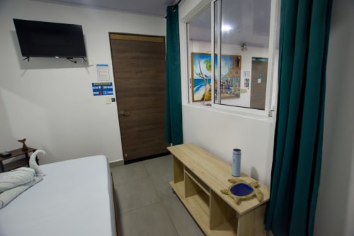 Dormitorio moderno en Vamos pa San Andrés Isla BnB con TV, escritorio de madera, cortinas turquesas y ventana con vista al jardín