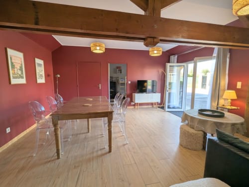 La chambre Carmen du Clos d'Émilie avec ses murs roses, table de salle à manger en bois, chaises transparentes et vue sur le jardin à Saint-Marcel