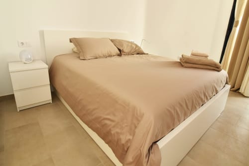 Dormitorio beige con mesita blanca y cortinas con vistas al mar en Sunset House, El Cotillo