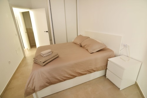 Dormitorio moderno y luminoso en Sunset House, El Cotillo con ropa de cama beige, mesita blanca y acceso al baño privado