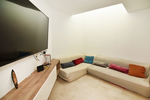 Acogedora sala de estar con sofá en L color crema, cojines coloridos, televisor de pantalla plana, escritorio de madera y luz natural abundante al atardecer