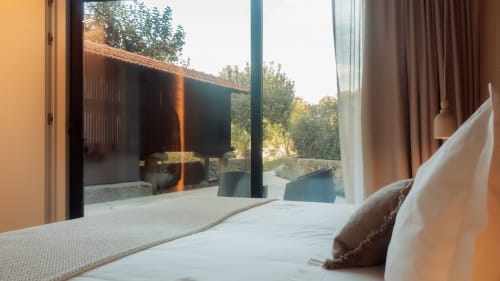 Dormitorio moderno en Quinta Das Pirâmides con ropa de cama blanca, vistas a la montaña a través de puertas de vidrio y diseño contemporáneo
