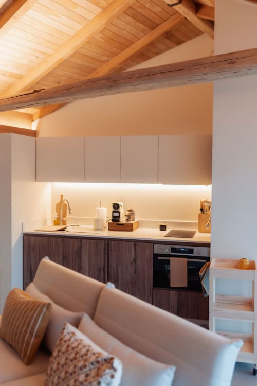 Cocina moderna con vigas de madera vista, muebles oscuros e iluminación LED cálida en la villa Celeiro de Quinta Das Pirâmides