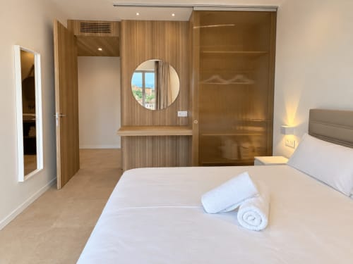 Moderno dormitorio del apartamento Holibai Baiona con armario de madera, espejo circular y vistas a la ciudad