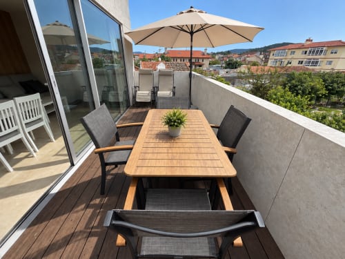 Soleada terraza en la azotea de Holibai en Baiona con mesa de comedor de madera, tumbonas y vistas a la ciudad
