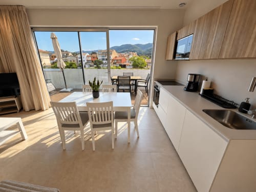 Moderno apartamento luminoso con cocina abierta y zona de comedor que se abre a la terraza soleada con vistas a la ciudad de Baiona y las montañas.