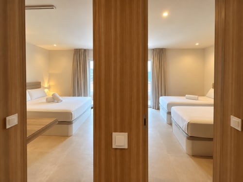 Dos modernas habitaciones de hotel con marcos de puertas de madera, camas blancas, iluminación cálida y vistas a la ciudad en apartamento de Baiona