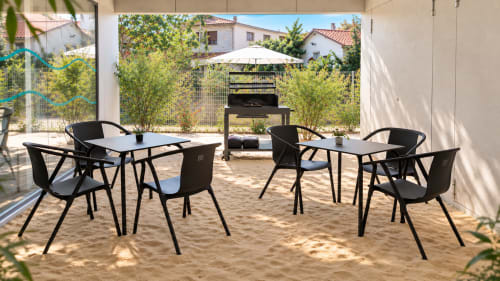 Terraza moderna al aire libre en el apartamento Holibai de Baiona con mesas de comedor negras, sillas y parrilla bajo condiciones soleadas