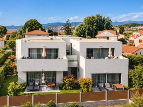 Modernos apartamentos blancos con terrazas en Baiona, España. Unidades duales con espacios exteriores amueblados, sombrillas y vistas a la ciudad.