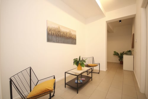 Soggiorno moderno in appartamento a Palermo con poltrona gialla, tavolino nero, pianta in vaso e opera d'arte forestale su sfondo bianco