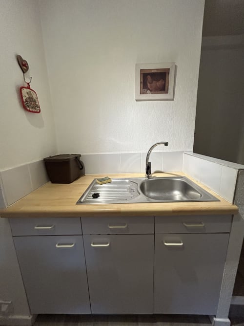 Kitchenette compacte dans un studio à Hébergement Luxeuil Les Bains avec évier, cuisinière, comptoir en bois et rangements