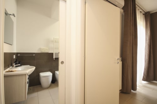 Bathroom entrance in Palermo deluxe apartment with sink, toilet, towel rack, and adjoining bedroom with curtains