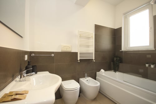Modern bathroom in Palermo apartment with white sink, toilet, bidet, bathtub and heated towel rack