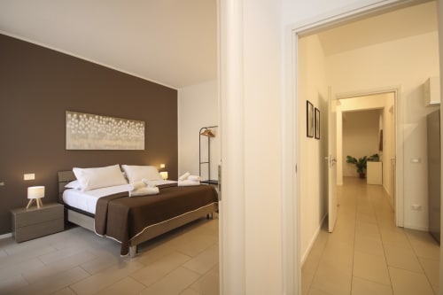 Deluxe bedroom apartment in Palermo with brown accent wall, queen bed, white pillows, wooden nightstand, and open doorway to