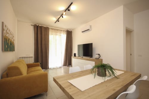 Modern Palermo apartment living room with yellow sofa, dining table, TV, plants, and bright windows