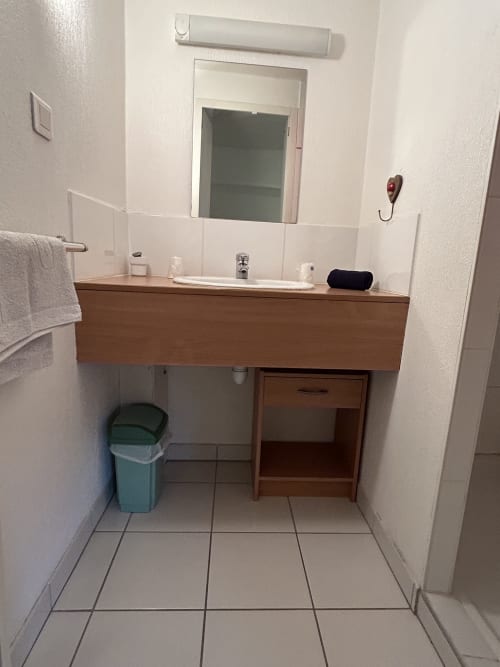 Salle de bains épurée avec meuble en bois, miroir et lavabo du studio Hébergement Luxeuil Les Bains en France