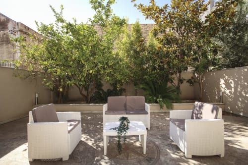 Sunny terrace at Location 10 Agency Palermo with white wicker seating, coffee table, and lush trees creating a peaceful