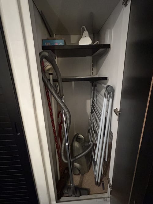 Petit placard utilitaire du studio Luxeuil Les Bains avec rangements, aspirateur, planche à repasser et fournitures ménagères