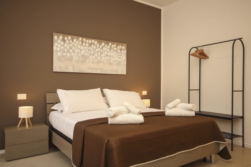 Deluxe bedroom in Palermo apartment with brown accent wall, white bedding, and modern furnishings
