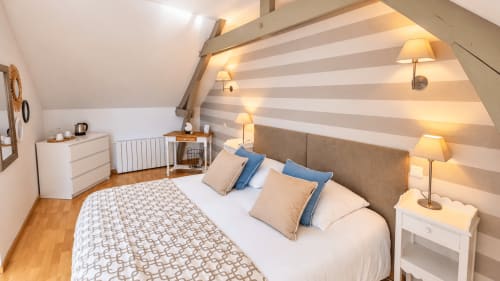 Lit double de la chambre Armor à Ty Coz Breizh, maison d’hôtes à Guidel, avec coussins bleus et beige, mur à rayures et poutres apparentes.