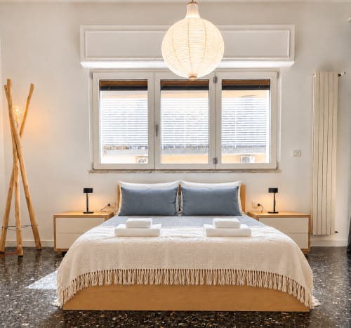 Camera moderna presso Easystay Bari con arredamento in legno, cuscini blu, lampada a sospensione e grandi finestre con vista sulla città