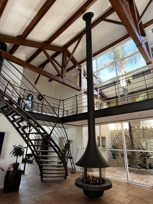 Intérieur de chambre d'hôte luxe avec cheminée centrale, poutres en bois, escalier mezzanine et puits de lumière à Capestang