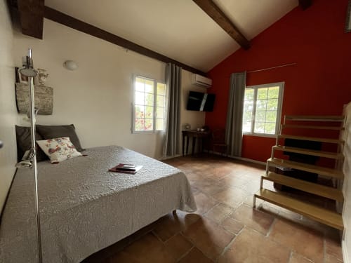 Chambre spacieuse aux Chambres d'hôtes la Soulenque avec mur accentué rouge, poutres en bois, carrelage terre cuite et vue sur jardin