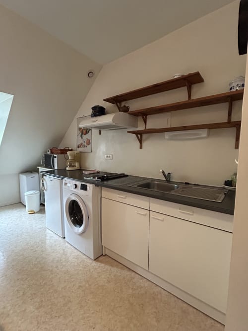 Kitchenette moderne avec armoires crème, plan de travail foncé, cuisinière au gaz, évier, étagères en bois et lave-linge au Duplex