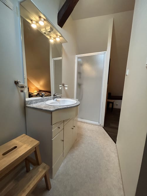 Salle de bains moderne avec lavabo, miroir éclairant et douche à l'appartement Hébergement Luxeuil Les Bains