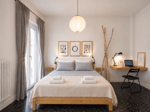 Camera moderna a Easystay Bari con letto in legno, lampada a sospensione, tende grigie, scrivania con laptop e arredamento minimalista.