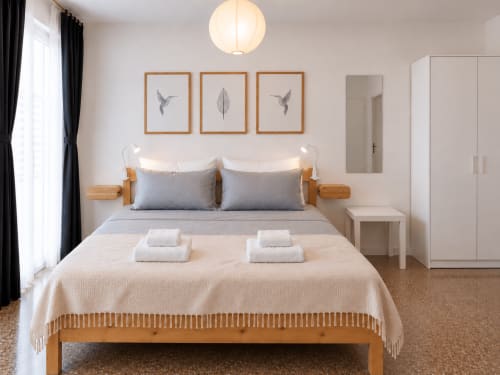 Camera moderna presso Easystay Bari con letto in legno, cuscini grigi, armadi bianchi e arte murale minimalista