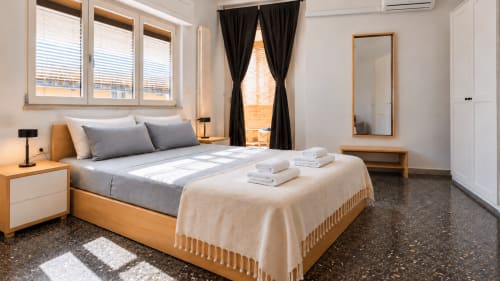 Camera spaziosa presso Easystay Bari con letto in legno, biancheria grigia, tende nere e arredi moderni con vista su Bari