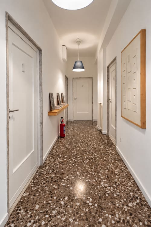 Corridoio moderno ad Easystay Bari con pavimento in terrazzo, porte bianche, illuminazione a sospensione e estintore