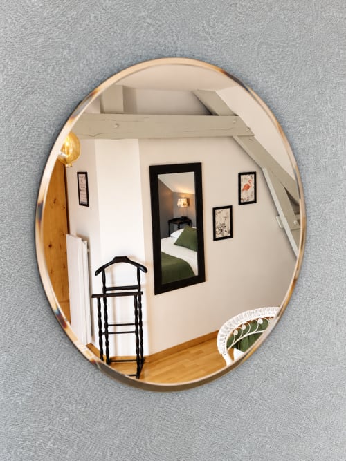 Miroir rond reflétant les poutres apparentes, le lit et la décoration aux flamants roses de la chambre Argoat à Guidel.
