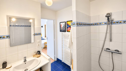 Salle de bain privative de la chambre familiale Heol à Guidel, avec douche, lavabo, miroir éclairé et carrelage bleu.