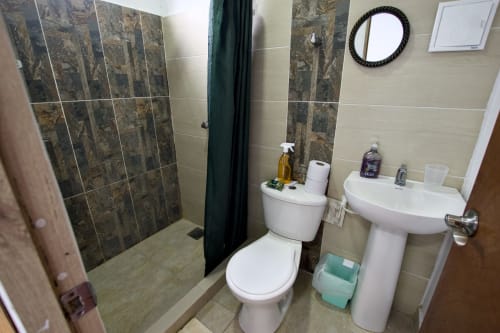 Baño moderno en Apto 301 Tiburones de Vamos pa San Andrés Isla con ducha de azulejos oscuros, lavamanos blanco pedestal e inodoro