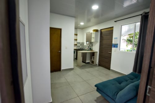 Sala de estar moderna con sofá azul turquesa, cocineta y piso de baldosas en Vamos pa San Andrés Isla BnB