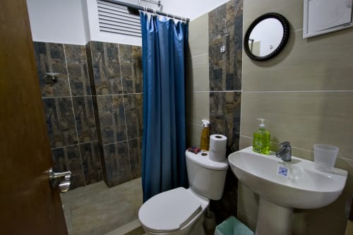 Baño moderno en cabaña Vamos pa San Andrés Isla con ducha alicatada, inodoro, lavamanos y cortina azul en San Andrés, Colombia