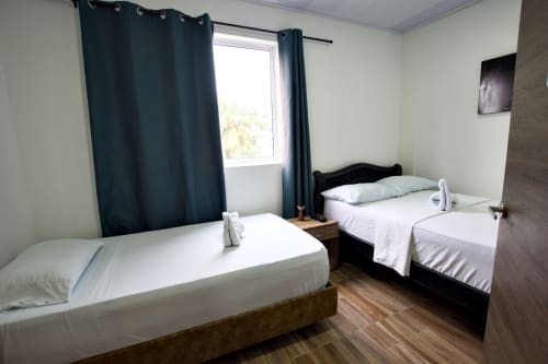 Luminosa habitación en Vamos pa San Andrés Isla con dos camas, cortinas oscuras, piso de madera y ventana con vista a las montañas