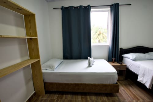 Luminosa habitación de cabaña en Vamos pa San Andrés Isla con dos camas, estantes de madera, cortinas oscuras y vistas a montañas tropicales