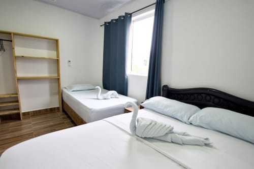 Espaciosa habitación en Vamos pa San Andrés Isla con dos camas, estantes de madera, cortinas oscuras y vistas a las montañas en San Andrés,
