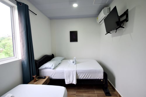 Habitación moderna en Vamos pa San Andrés Isla con camas gemelas, TV de pared, aire acondicionado y vista a las montañas desde la ventana