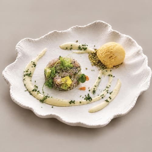 Elegant plated seafood dish at Ô Château hotel featuring seared fish, yellow sauce, and microgreens on white scallop-shaped