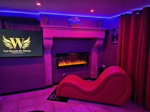 Chambre d'amour luxueuse aux Secrets de Winna avec canapé rouge incurvé néon, cheminée et ambiance lumineuse violette