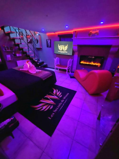 Chambre romantique aux Secrets de Winna avec éclairage violet vibrant, sièges en forme de cœur et ambiance cheminée