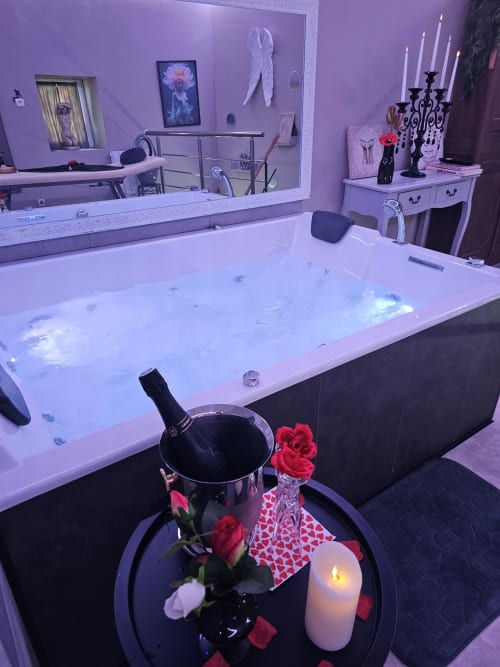 Luxueuse suite spa romantique avec baignoire balnéo illuminée, éclairage ambiant violet et décoration de roses chez Les Secrets de